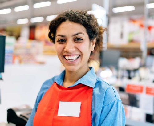 A smiling woman wearing an employees apron and name tag.