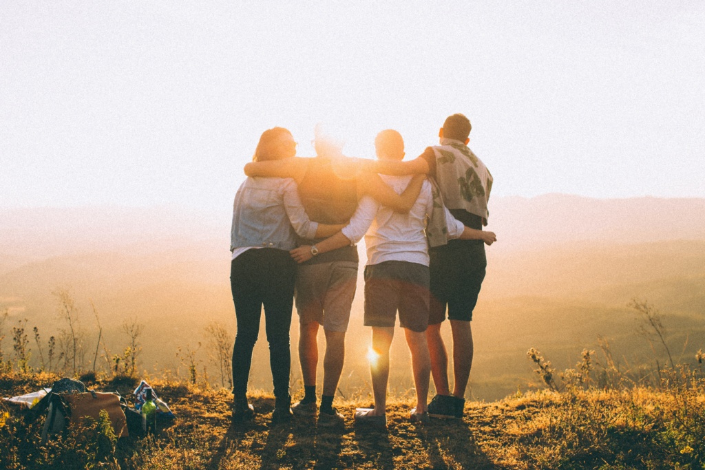 four people with their arms around each other looking towards the sunset